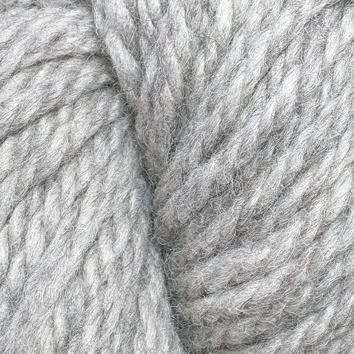 Close-up of thick, soft Halcyon Yarn Classic Rug Wool by Caledonian Dye Works in light grey. Strands are tightly twisted with a slightly fuzzy texture, highlighting the detailed fibers ideal for rug weaving. Available in skeins.