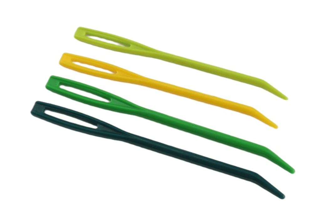 The Bryson Distributing, Inc. Plastic Tapestry Needles - 4 features four plastic curved tip needles in assorted green shades with large eyes and blunt tips, ideal for super bulky or eyelash yarns. Displayed diagonally on a white background.