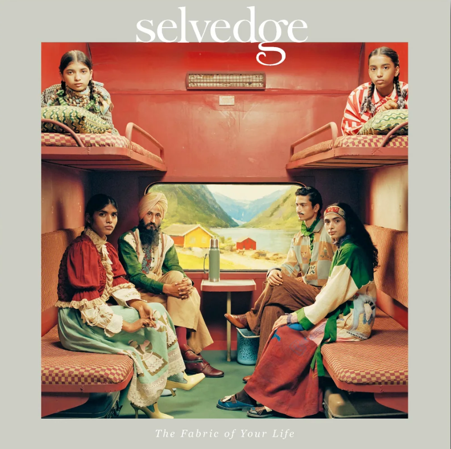 Six people sit in a train compartment featured in Selvedge Issue 133: Kin, with red upholstery and craft details, as a scenic mountain landscape reflecting local cultural heritage appears through the window.