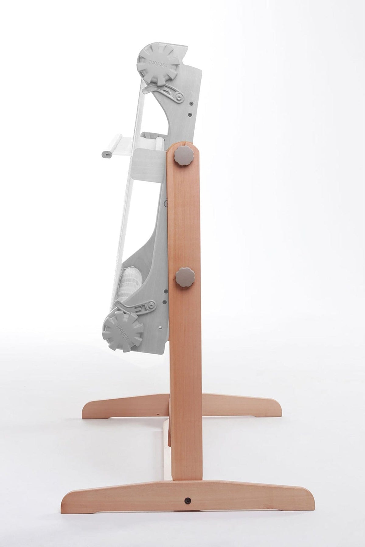 A side view of the Ashford Rigid Heddle Floor Stand by Ashford Handicrafts Limited highlights its wooden base, upright frame with metal parts and handle, and an ergonomic adjustable weaving angle, all set against a white background.