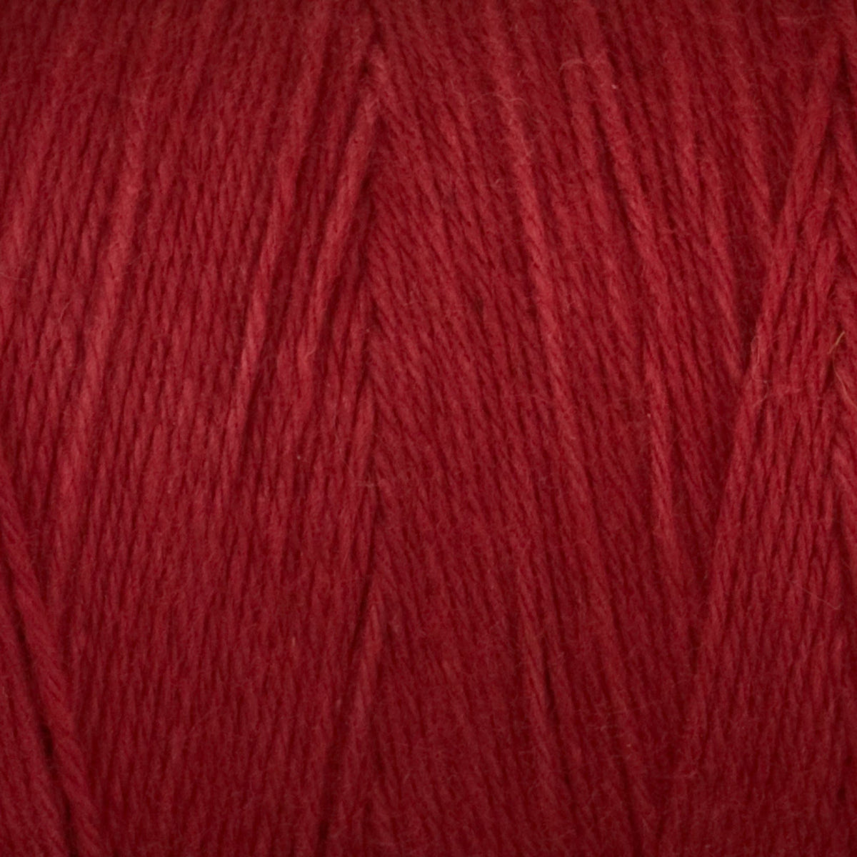 Close-up of Great Northern Weaving Cotton Carpet Warp 8/4: deep red 4-ply cotton yarn with soft fibers and loosely twisted strands, highlighting its textured surface and subtle color variations.