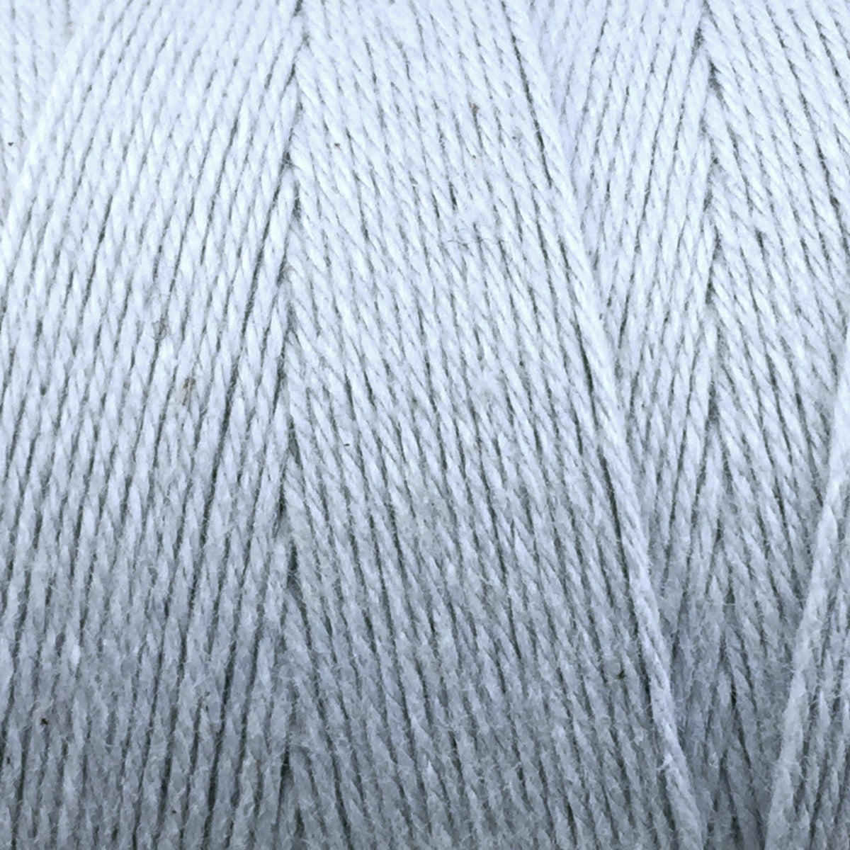 Close-up of Great Northern Weaving's Cotton Carpet Warp 8/4: white 4-ply cotton yarn wound in parallel layers on a spool, highlighting detailed fibers ideal for weaving strong, colorfast cotton yarn rugs.