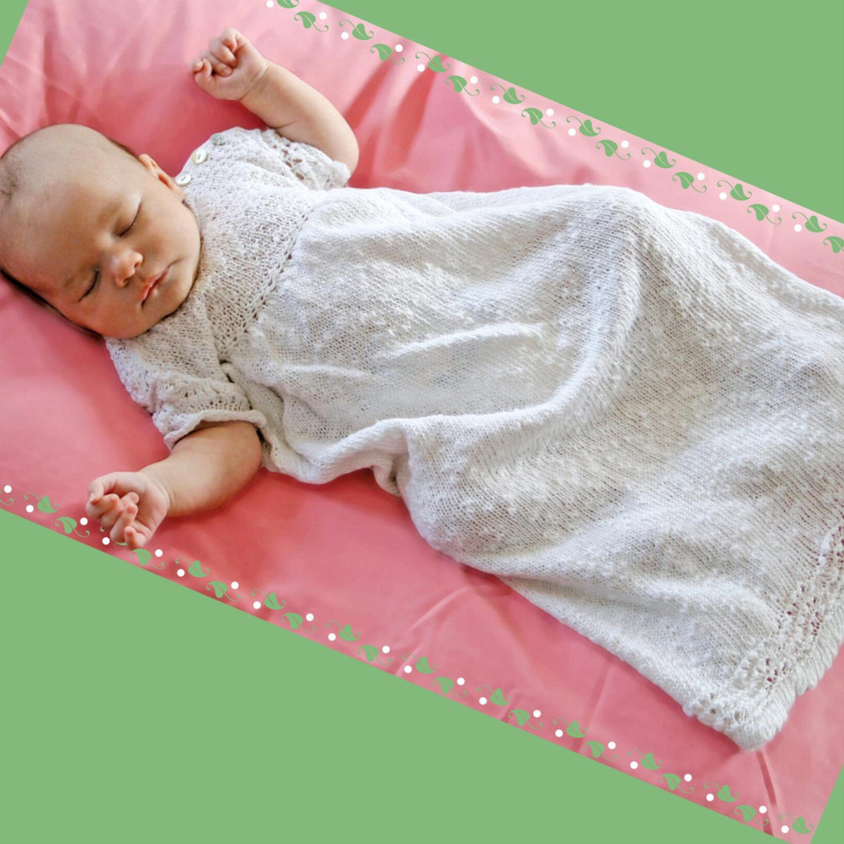 A baby in the Halcyon Yarn Heirloom Christening Gown sleeps peacefully on a pink floral-bordered blanket, set against a green background, highlighting the gown’s beautiful texture and the serenity of new life.