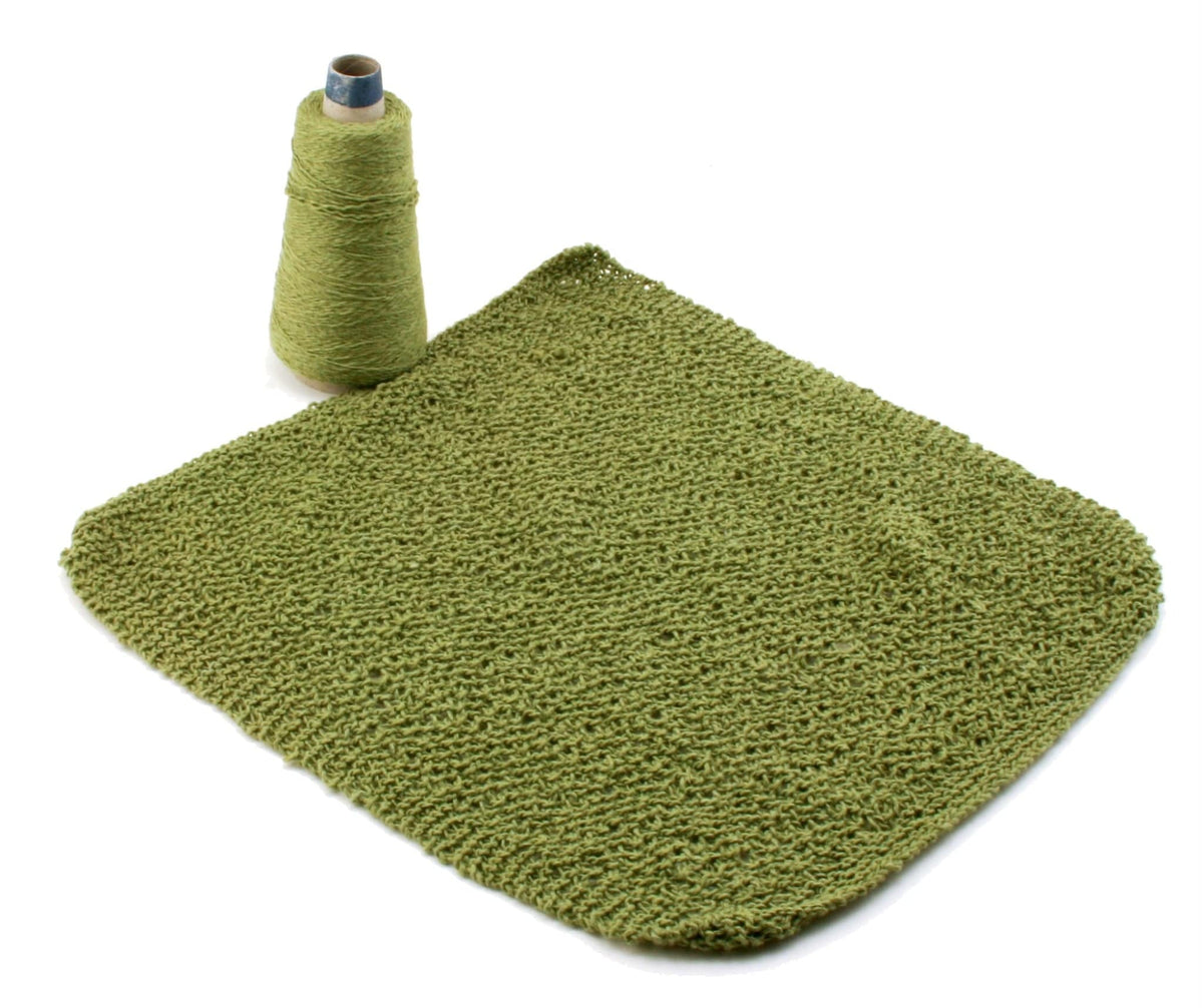 A spool of green Casco Bay Sport yarn is paired with a textured green washcloth, both from Halcyon Yarn’s Casco Bay Washcloths collection, displayed on white—a great source of washcloth pattern inspiration.