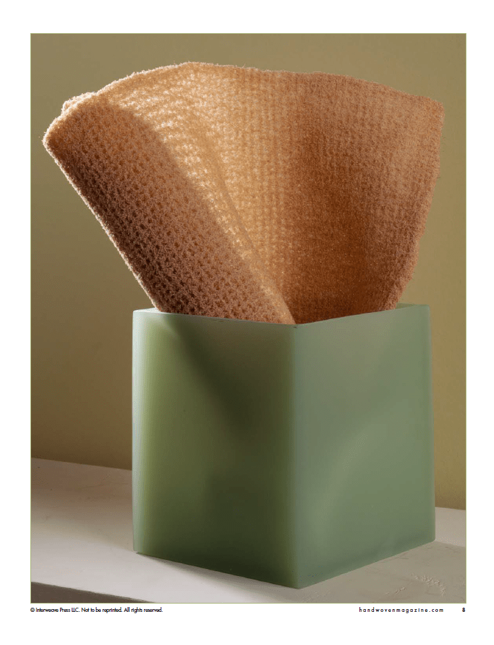 A textured, light brown cleaning cloth in a frosted green square container sits against a neutral background—perfect inspiration for your next project with "Winning Towels from Handwoven's 21st-Century Towel Contest" eBook by Long Thread Media.