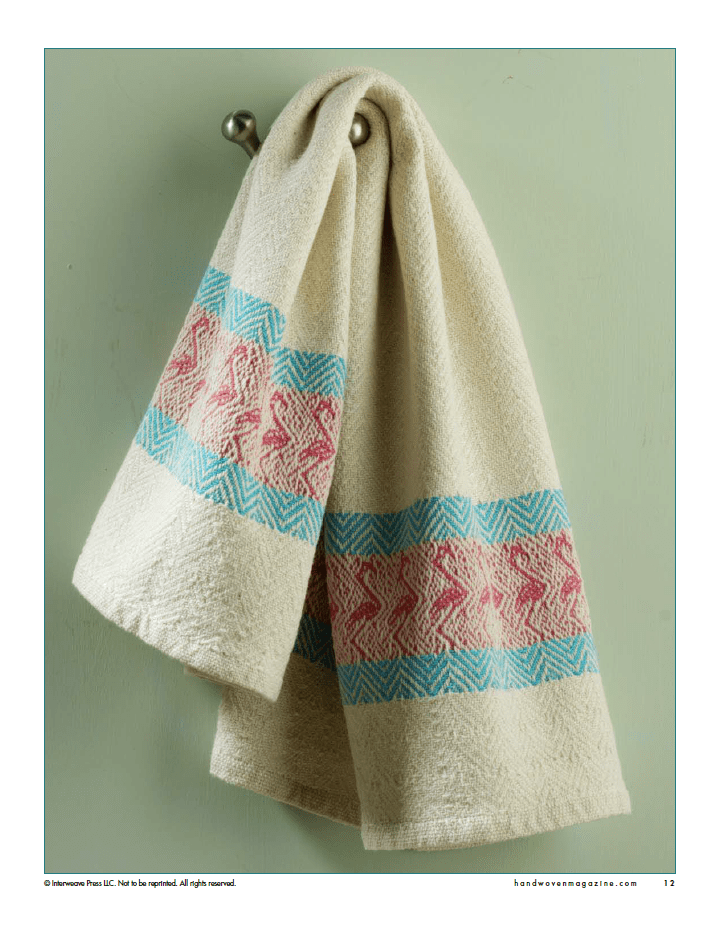 A cream-colored, handwoven towel from Long Thread Media's Winning Towels (Handwoven's 21st-Century Towel Contest, eBook Printed Version) hangs on a silver hook, showing pink and blue geometric bands against a pale green wall.