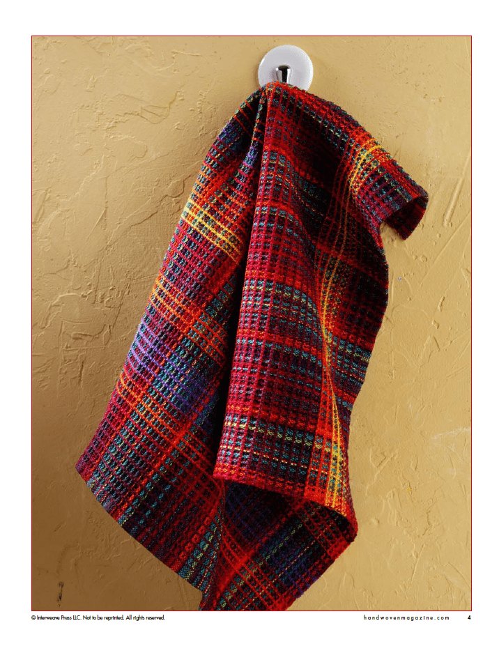 A vibrant plaid towel hangs on a white hook against a tan wall—perfect inspiration from Long Thread Media’s "Winning Towels from Handwoven's 21st-Century Towel Contest" (eBook Printed Version).