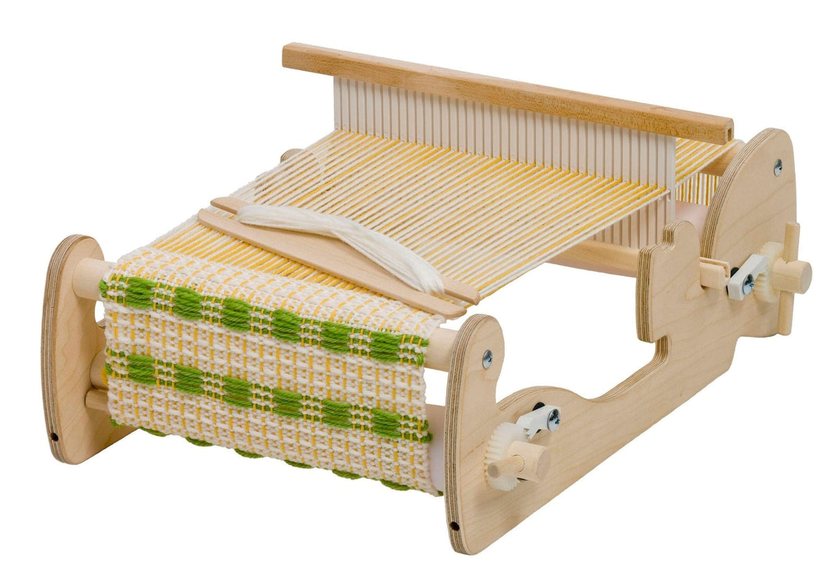 A Schacht Spindle Co. Cricket Rigid Heddle Loom (approx. 5 week delivery), shown set up as a portable wooden weaving loom with yellow and white threads, is pictured weaving a fabric that features a white base accented with green and yellow patterns.