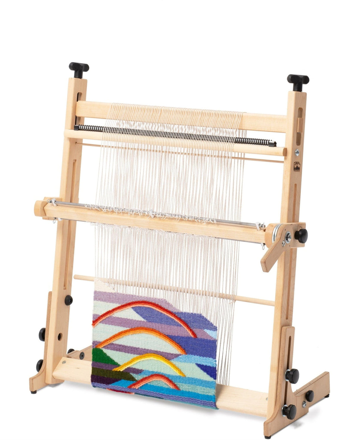 The Arras 20″ Tapestry Loom by Schacht Spindle Co. stands upright with a partially completed, colorful abstract fabric in blue, yellow, orange, and red. White warp threads are visible above the woven portion, clearly illustrating precise tension control throughout the weaving process.