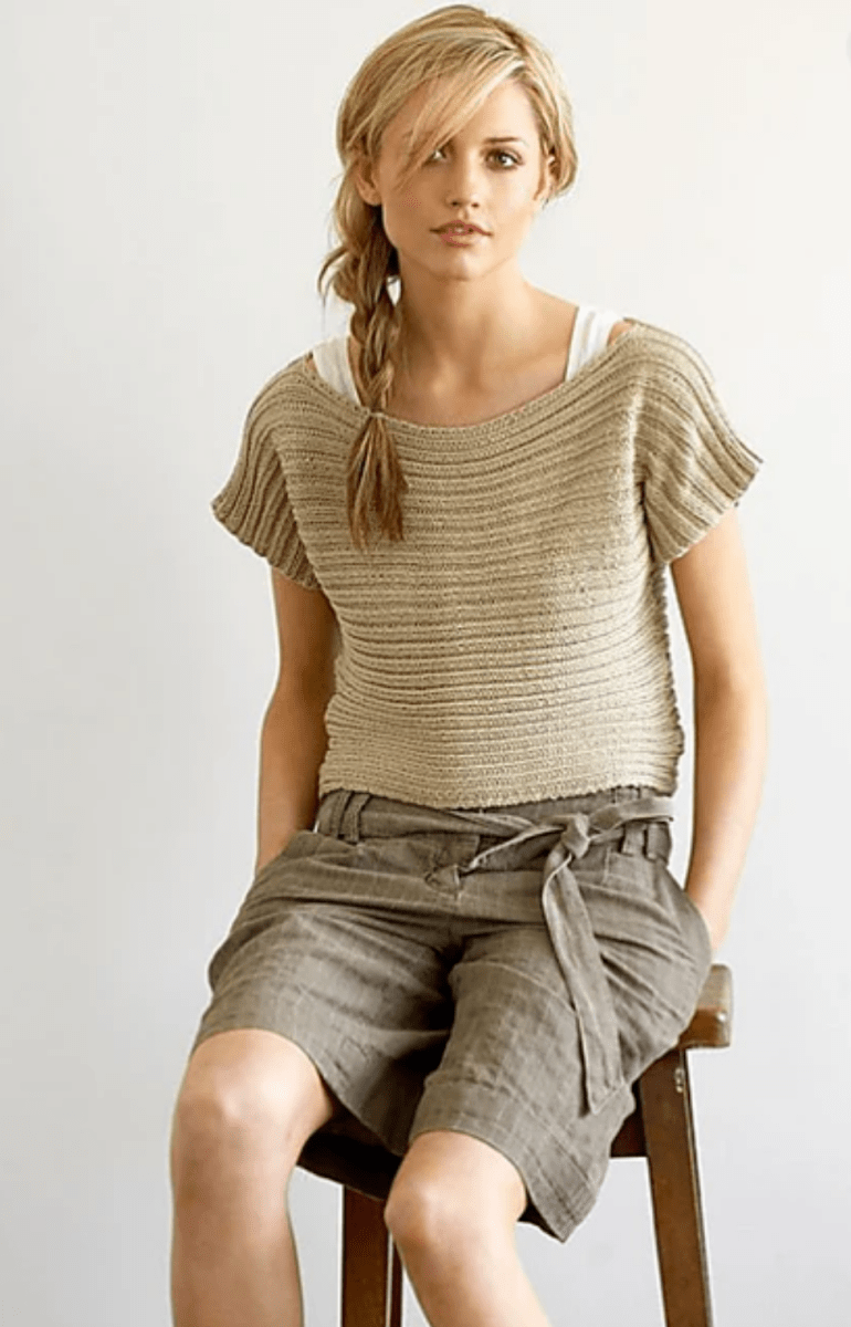 A woman wearing a tan, horizontally ribbed Sideways Ribbed Top Pattern top and dark brown shorts while sitting on a wooden stool.