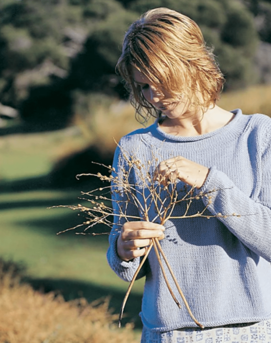 A woman in a light blue Somerville Sweater, by Jo Sharp, holds a bundle of dried twigs.