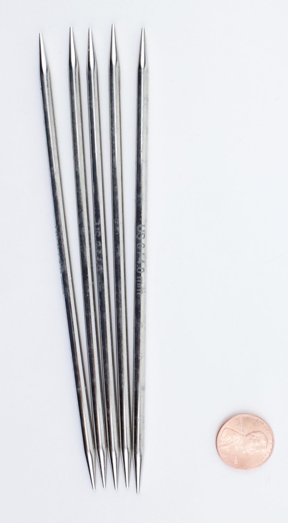 Five Accessories Unlimited Knit Pro Nova Metal Double-Point Knitting Needles, 6" each, are fanned out beside a penny for size comparison on a plain white background.
