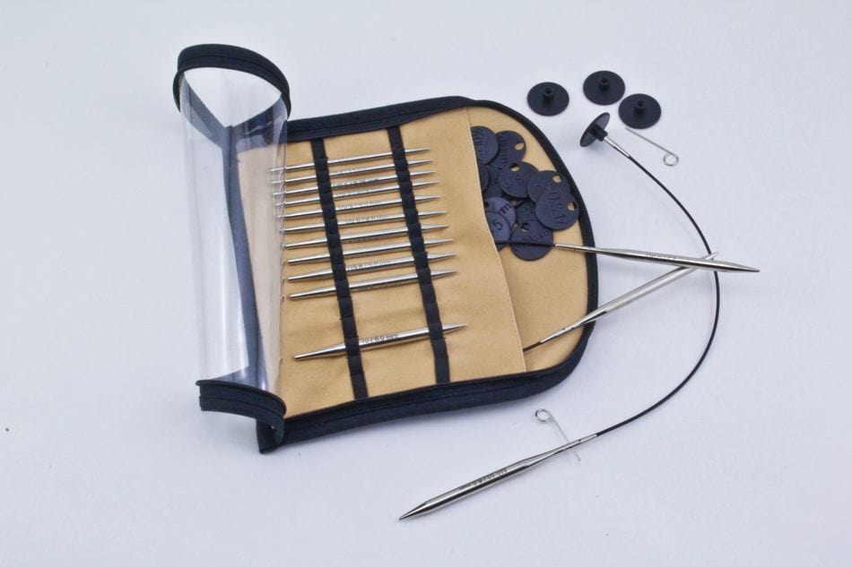 The Accessories Unlimited Knit Pro (Knitters Pride) Nova Metal Interchangeable Circular Knitting Needle Set features chrome-plated needles with metal tips, black cables and end caps, in a beige case with a transparent cover.