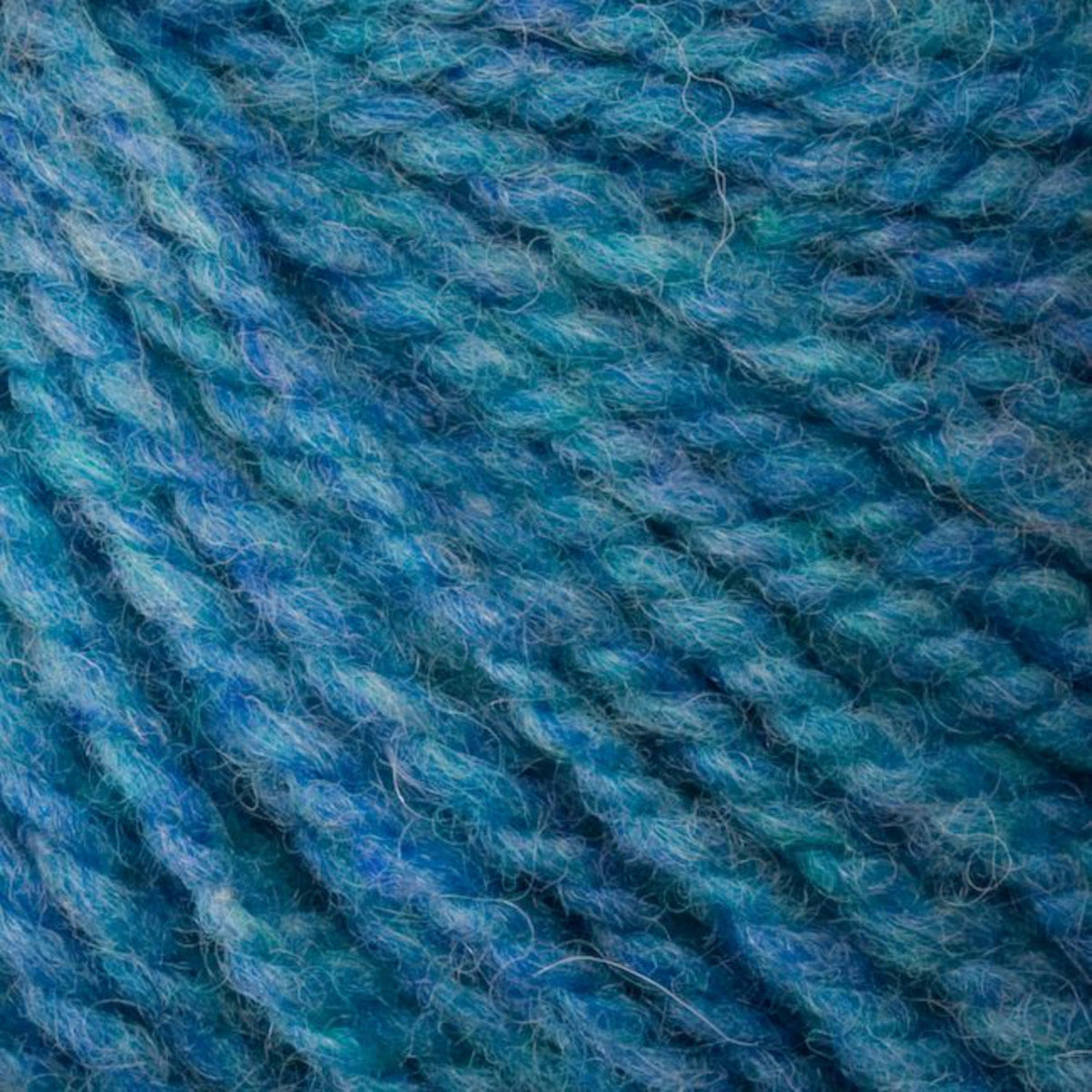 Close-up of the intricately twisted blue and teal fibers of Bartlettyarns' Bartlett Maine Wool, Sport Weight Cones, creating a textured pattern with hints of green that enhances its homespun charm.