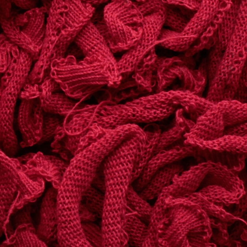 A close-up view showcases a collection of red Harrisville Potholder Loops in traditional size by Friendly Loom, featuring a textured and intertwined appearance. These loops form intricate patterns reminiscent of work on a traditional loom, offering the image a rich and vibrant color.