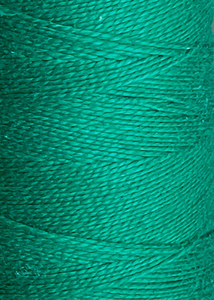 Close-up of green thread wound tightly around a spool, highlighting the detailed texture and fine fibers of the 3/2 Looma Circulo Mercerized Pearl Cotton Yarn | Large Cone by Circulo, which is Oeko-Tex certified for safety and quality.