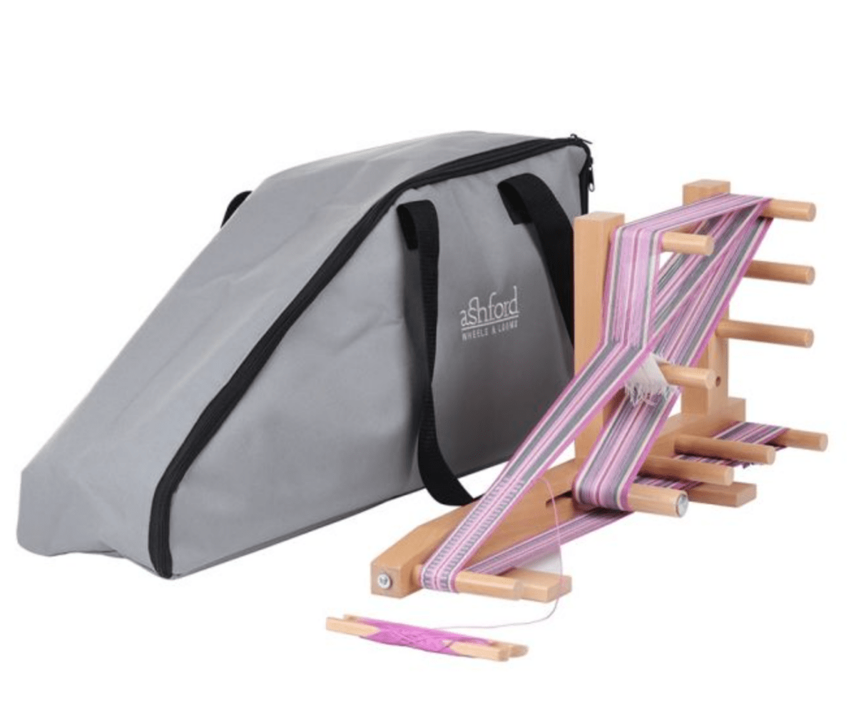 The Ashford Inkle Loom Carrying Bag from Ashford Handicrafts Limited is shown with a tabletop inkle loom featuring pink and purple woven bands, and comes in gray with sturdy black handles.