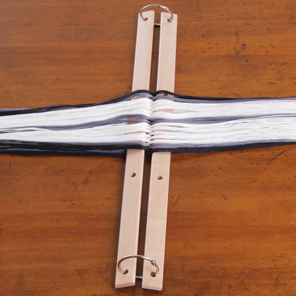 Two Ashford Cross/Warp Sticks for Table Loom by Ashford Handicrafts Limited, each with metal rings at both ends, hold parallel black and white yarn on a brown wooden surface—essential for setting up your weaving warp.