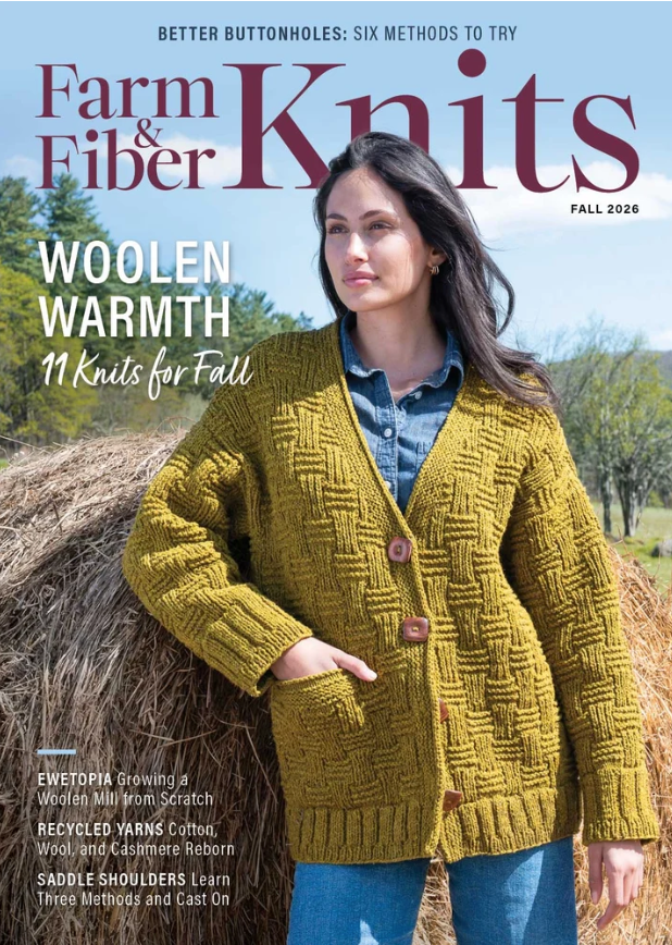 A woman dressed in a yellow knit cardigan and denim shirt stands before stacked hay bales. The cover of Farm & Fiber Knits Magazine, Fall 2026 by Long Thread Media showcases themes of woolen warmth, fall knitting patterns, and sustainable yarns.