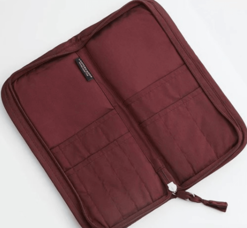 The maroon Lantern Moon DPN Needle Case by Bryson Distributing, Inc. is open, displaying multiple inner pockets and compartments for organization, a quilted IKAT fabric lining inside, and a stitched fabric tag near the top.