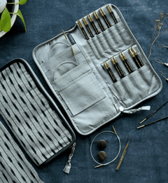 An open handcrafted Lantern Moon Interchangeable Needle Case by Bryson Distributing, Inc. sits on a blue surface, neatly organizing knitting needles, crochet hooks, and cables. Nearby are a closed matching case, yarn, and accessories.