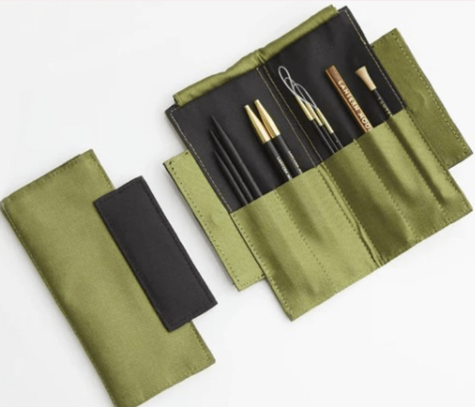 The Lantern Moon Mindy Sleeve by Bryson Distributing, Inc. is a green silk blend case with a black flap, shown closed (left) and open (right), storing assorted pencils, pens, and a paperclip in stitched compartments.