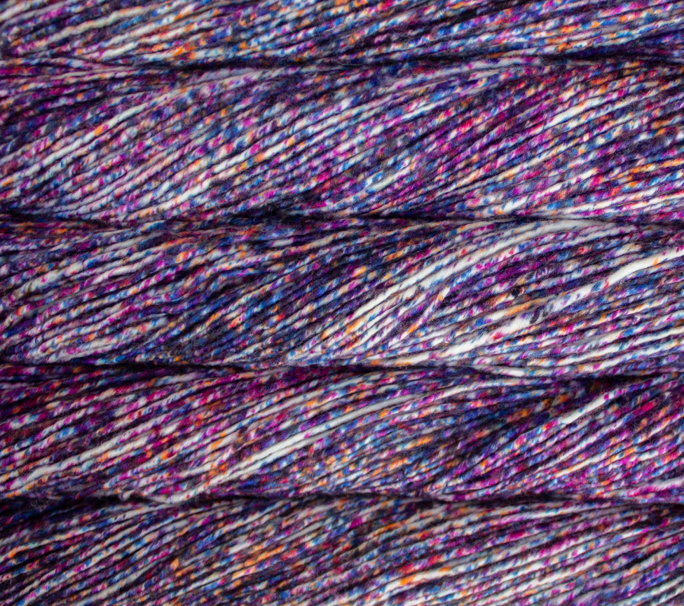 Close-up of stacked skeins of Malabrigo Mecha hand dyed bulky yarn in shades of deep purple, blue, magenta, and white.