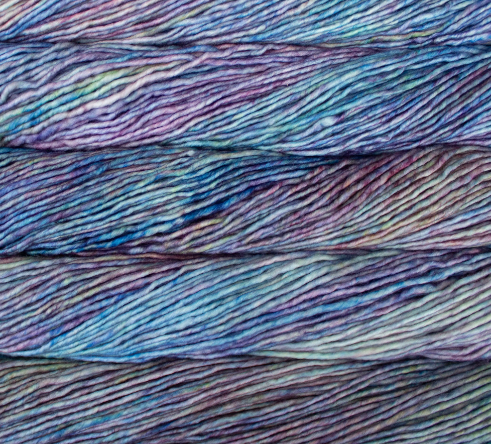 Several skeins of Malabrigo Mecha hand-dyed superwash yarn featuring a variegated pattern of purple, blue, and pale green tones.