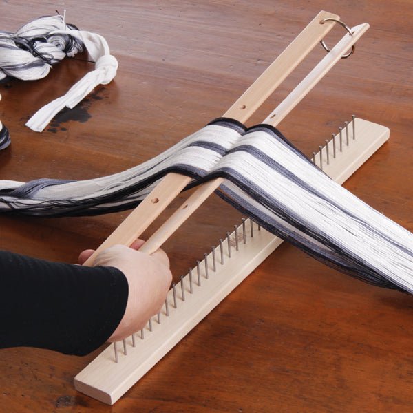 A person organizes and separates black and white yarn for weaving using Ashford Cross/Warp Sticks for Table Loom by Ashford Handicrafts Limited on a wooden tabletop.