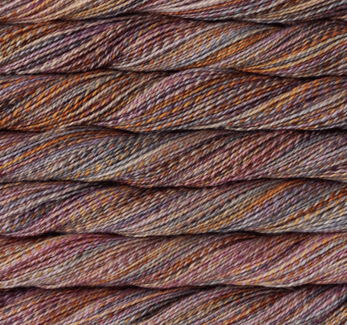 Close-up of stacked skeins of Malabrigo Torzal hand-dyed sport weight yarn in variegated shades of purple, orange, brown, and grey.