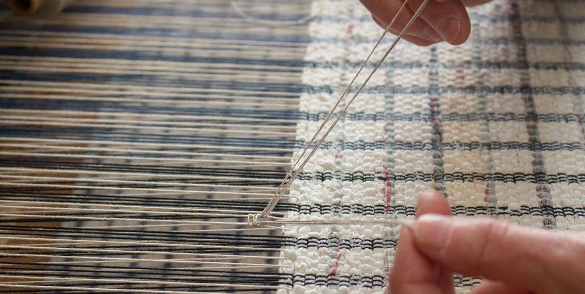 A close-up of hands using a needle to weave light-colored thread into textured fabric on a loom for VÄV Bookazine 2026, capturing a Scandinavian textile tradition.