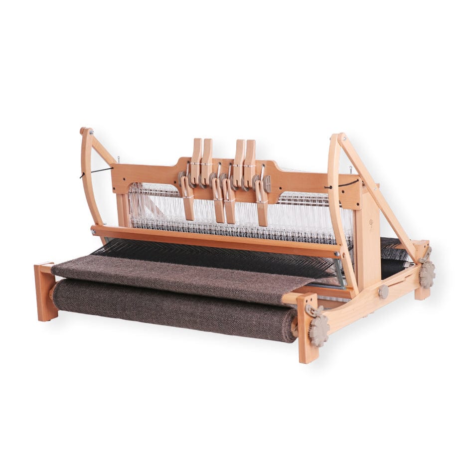 An Ashford Handicrafts Limited Ashford Table Loom, featuring an overhead swinging beater and shuttle race, displays dark woven fabric on the front beam, isolated on a white background.
