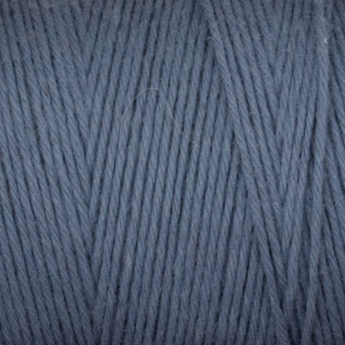 Close-up of blue-grey Great Northern Weaving Cotton Carpet Warp 8/4 yarn, highlighting the tightly twisted 4-ply cotton strands. This colorfast, soft, and smooth yarn is perfect for weaving or rug making projects.