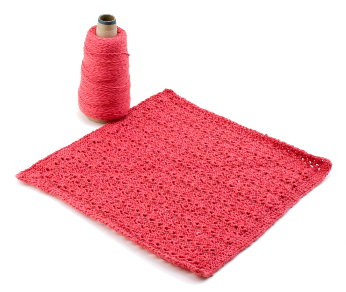 A spool of pink sport weight cotton yarn sits beside a pink, lace-patterned swatch—ideal for washcloths—featuring the "Casco Bay Washcloths, download" pattern by Halcyon Yarn, displayed on a white background.