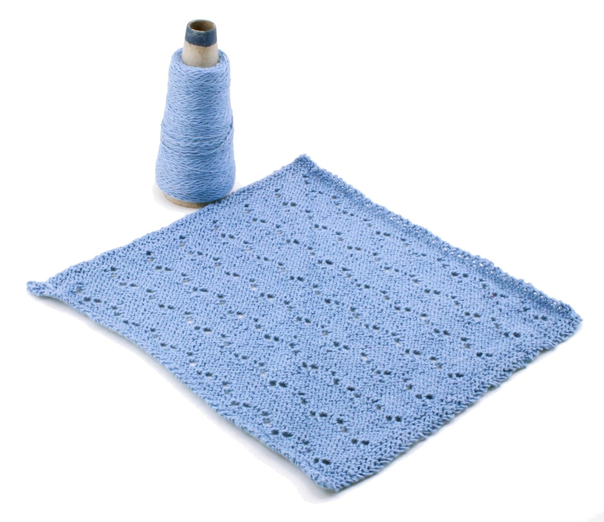 A spool of light blue sport weight cotton yarn from Halcyon Yarn sits beside a knit swatch with eyelets, showcasing the Casco Bay Washcloths pattern (download), displayed on a white background.