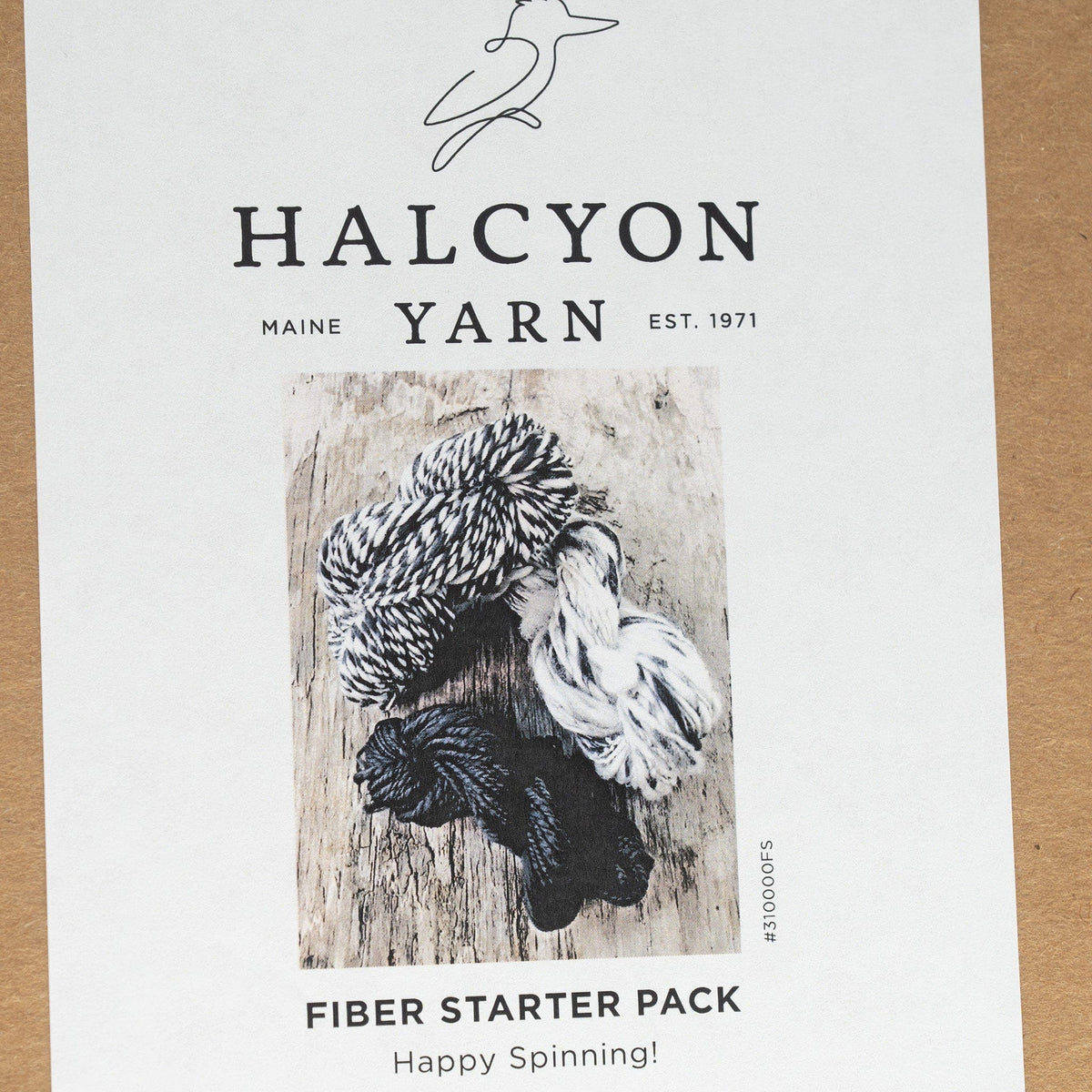 A label for Halcyon Yarn Fiber Starter shows three skeins—black, white, and black-and-white twisted yarn—on a rustic wooden background. Ideal for spinning wool, with the text: Happy Spinning!.