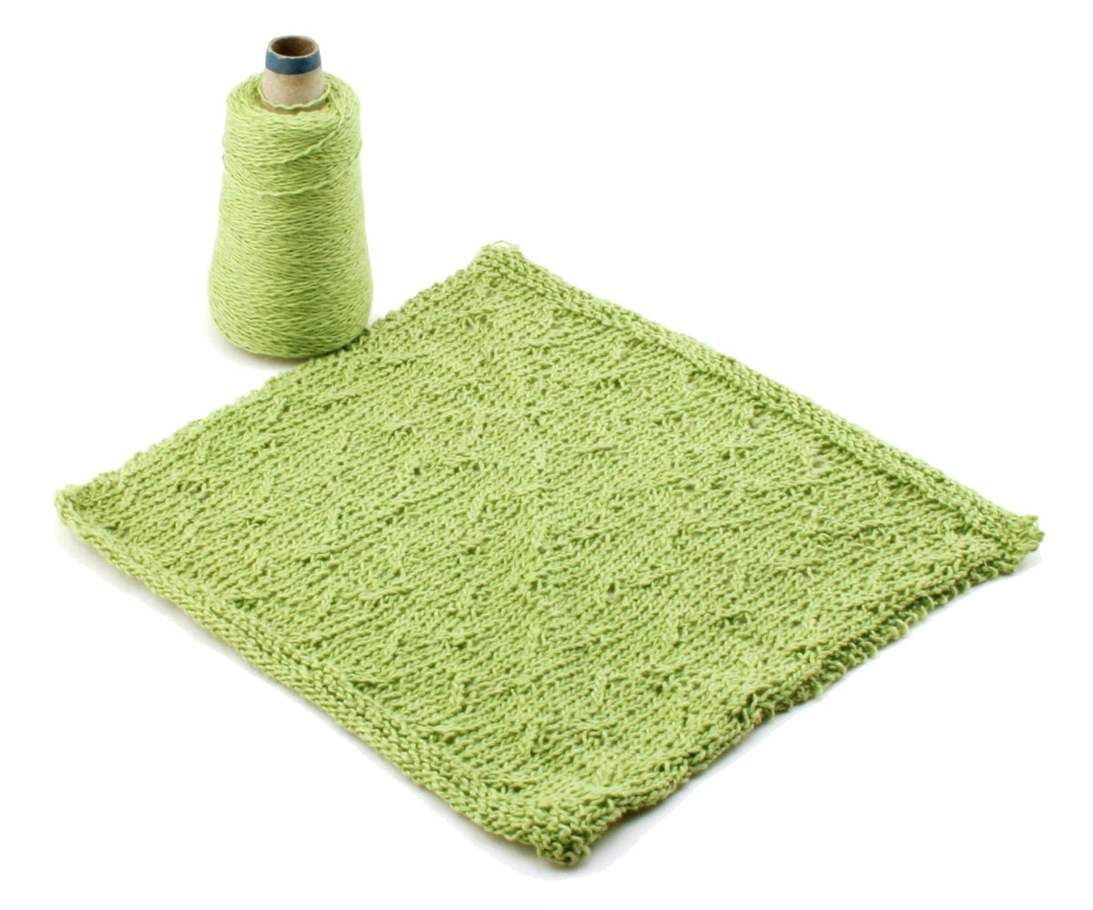 A skein of Halcyon Yarn Casco Bay Washcloths in light green sits beside a textured knitted swatch, both displayed on a white background.