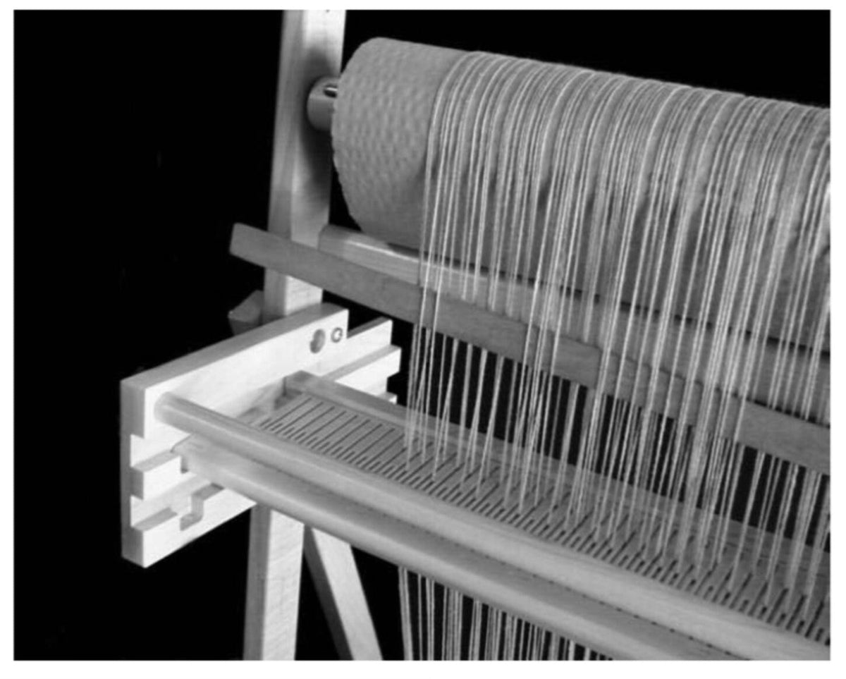 A close-up of the Leclerc Penelope III 22.5″ Rigid Heddle Tapestry Loom with two rigid heddles shows threads stretched vertically on its wooden frame against a dark background.
