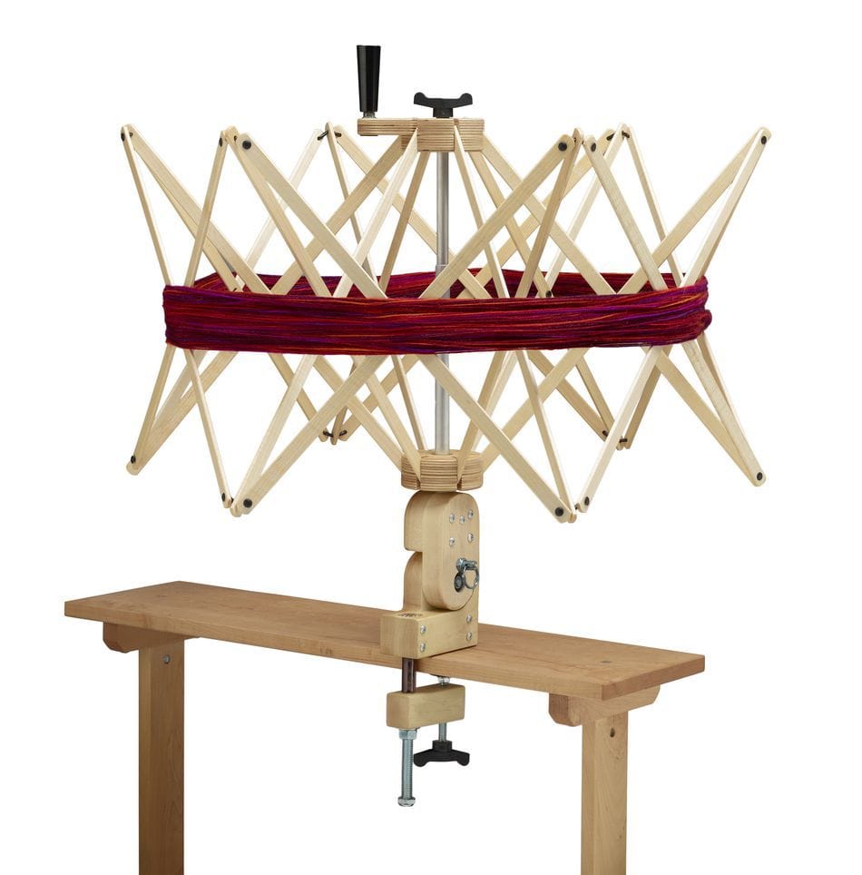 A Schacht Spindle Co. Ultra Umbrella Swift—currently out of stock at Schacht—clamps to a table and expands its arms into a circular frame, holding a skein of red yarn to keep it untangled while winding.
