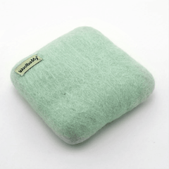The Woolbuddy Felting Mat, Small is a light green, square 100% wool mat with rounded edges and a woolbuddy tag—ideal for needle felting projects. Shown on a plain white background. Brand: Woolbuddy.