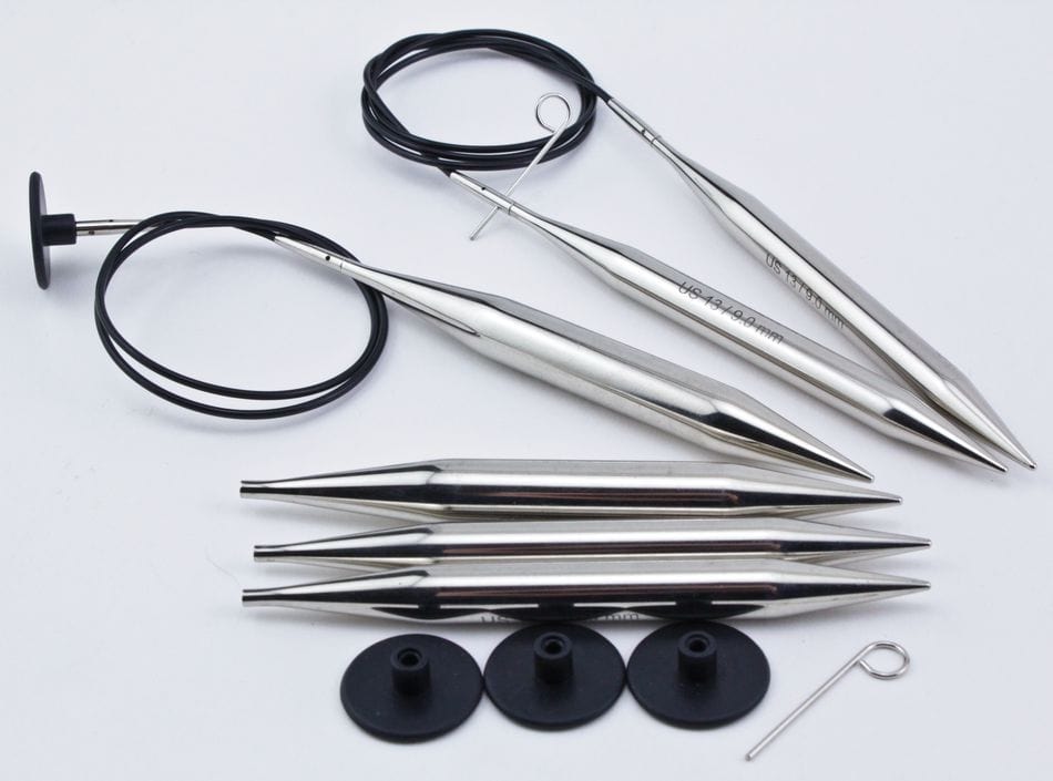 The Accessories Unlimited Knit Pro (Knitters Pride) Nova Metal Interchangeable Circular Knitting Needle Sets include chrome-plated pointed needles, black cables, end caps, and a metal tightening key, arranged on a white surface.