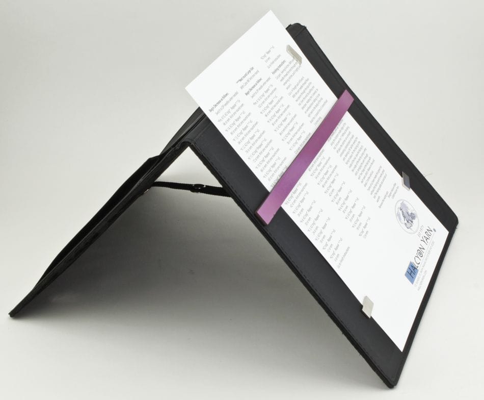 The Magnetic Pattern Holder by Knit Pro (Knitters Pride) from Accessories Unlimited holds a sheet upright with metal clips and a purple bar, displayed on a black angled stand against a plain white background.