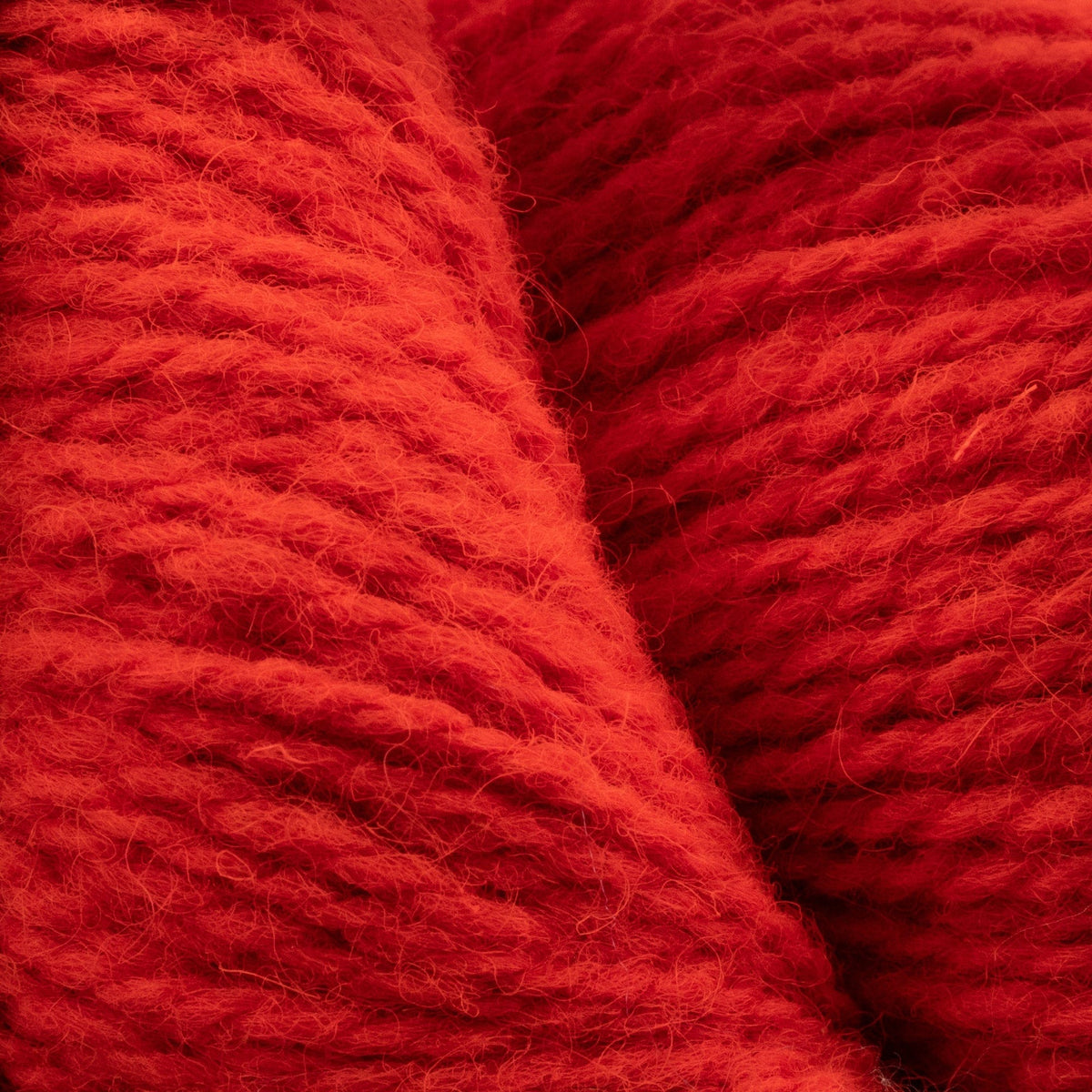Close-up of Bartlettyarns Maine Wool Yarn (Fisherman 2-Ply) by Bartlettyarns in red, highlighting the thick, fuzzy worsted weight fibers and twisted strands in detail.