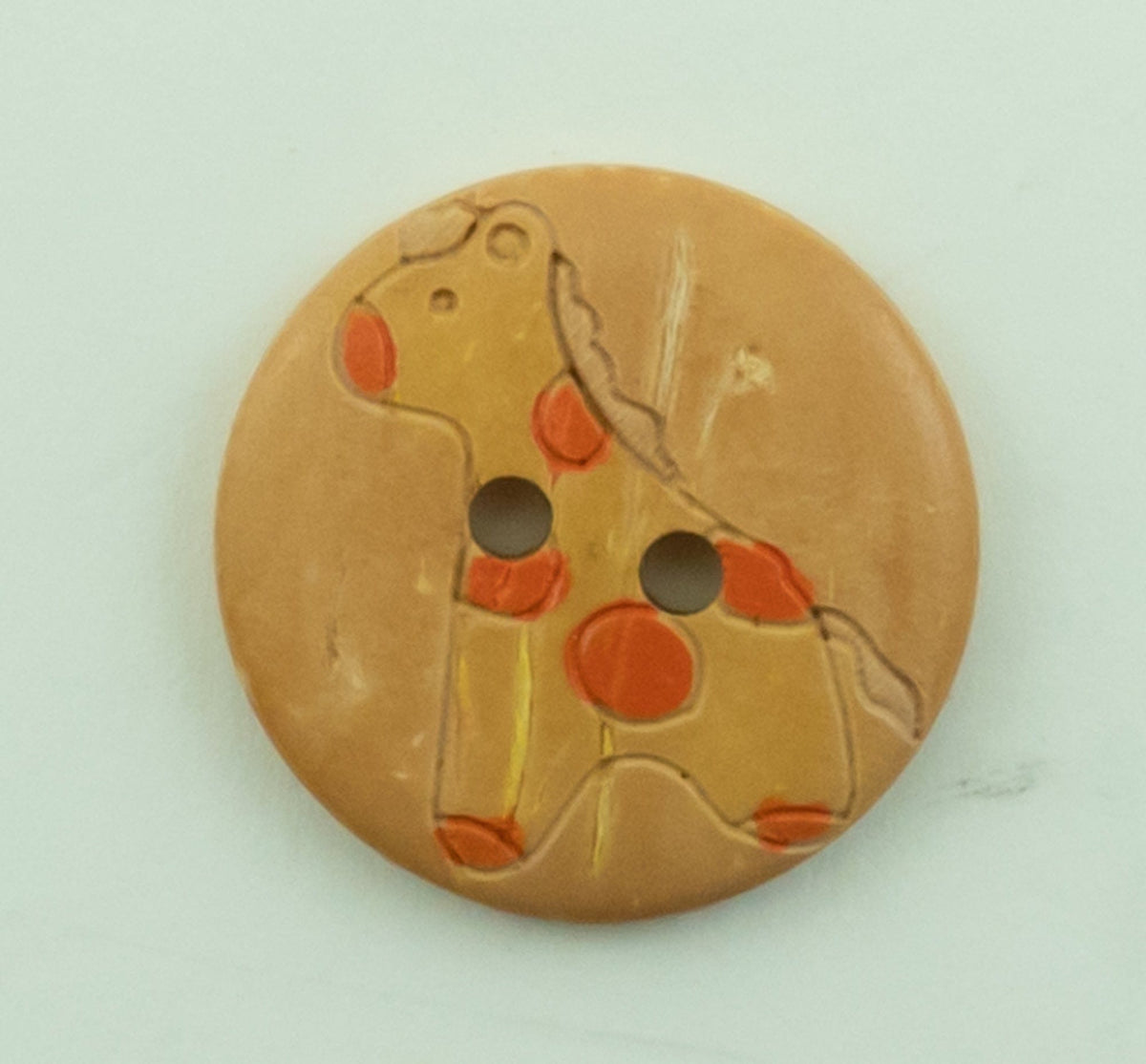 The Buttons Etc. Baby Animal Button, 13/16", features a cartoon giraffe with orange spots painted on tan and has two center sewing holes.