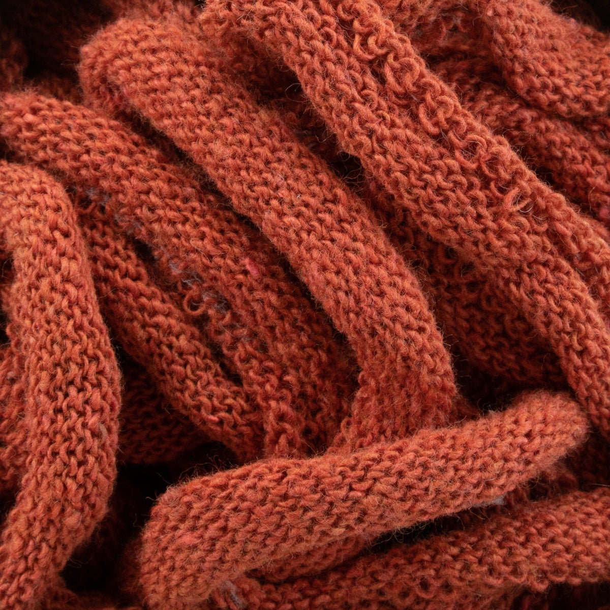 Close-up of tangled Harrisville Potholder Loops - Traditional Size from Friendly Loom, featuring orange fabric strands forming a dense, intertwined pattern reminiscent of traditional weaving. The texture appears soft and woolly, showcasing the intricate design and warm hue.